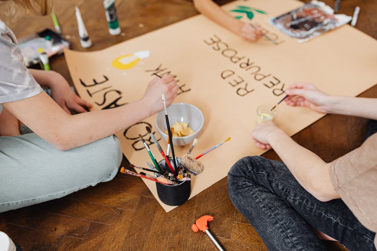 People collaborating on a colorful environmental poster using paints and brushes.